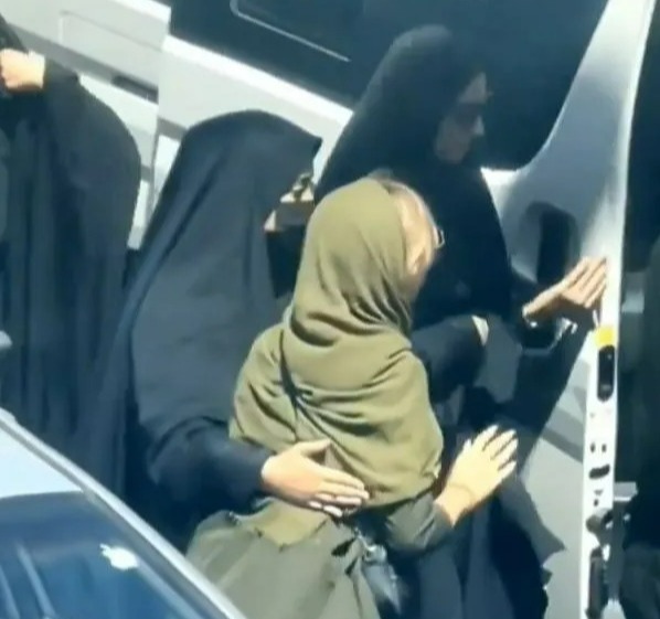 The women in green is led towards an open van on a busy road in Iran