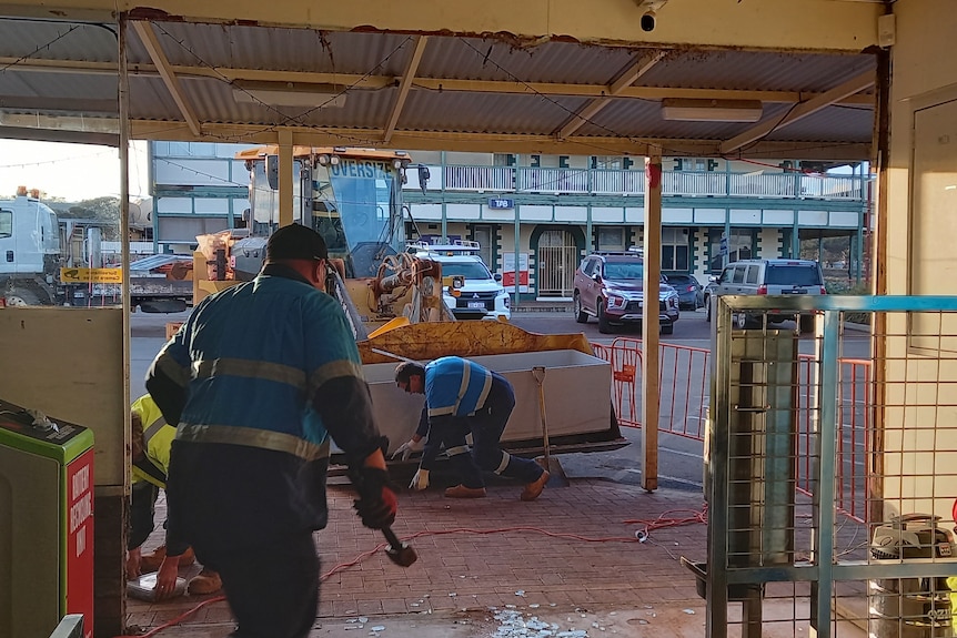 Workers repairing damage to a supermarket entrance after a ram raid. 