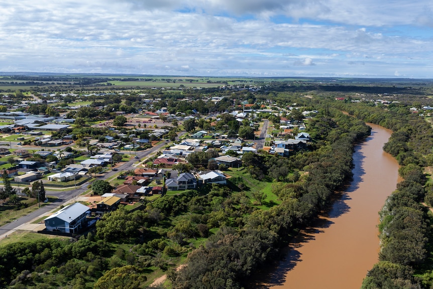 An aerial shot of an outback town with a brown river. 