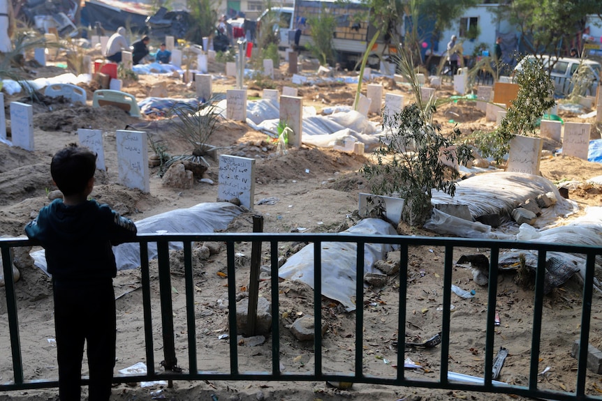 A small child looks at mass graves. 