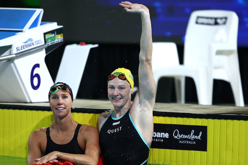 Cate Campbell waves to the crowd alongside Emma McKeon in the pool