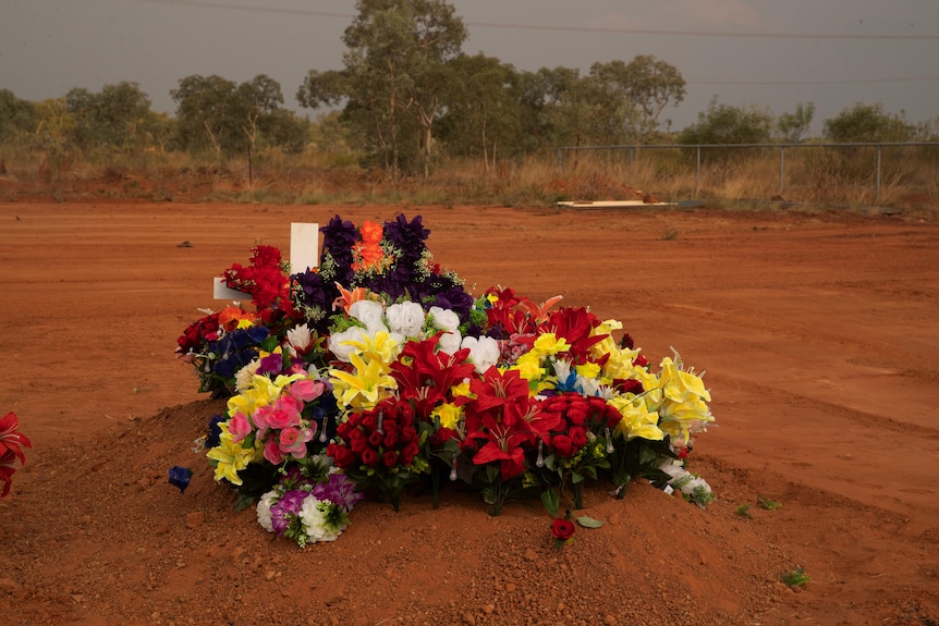 A single grave adorned with flowers lies among the red earth