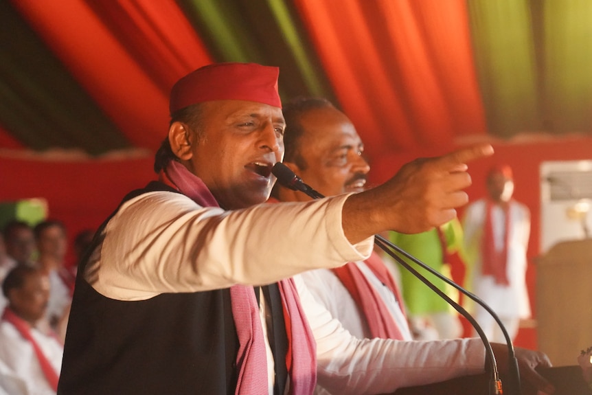 A close up of an Indian man at a lecturn speaking into a microphone and pointing to the crowd.