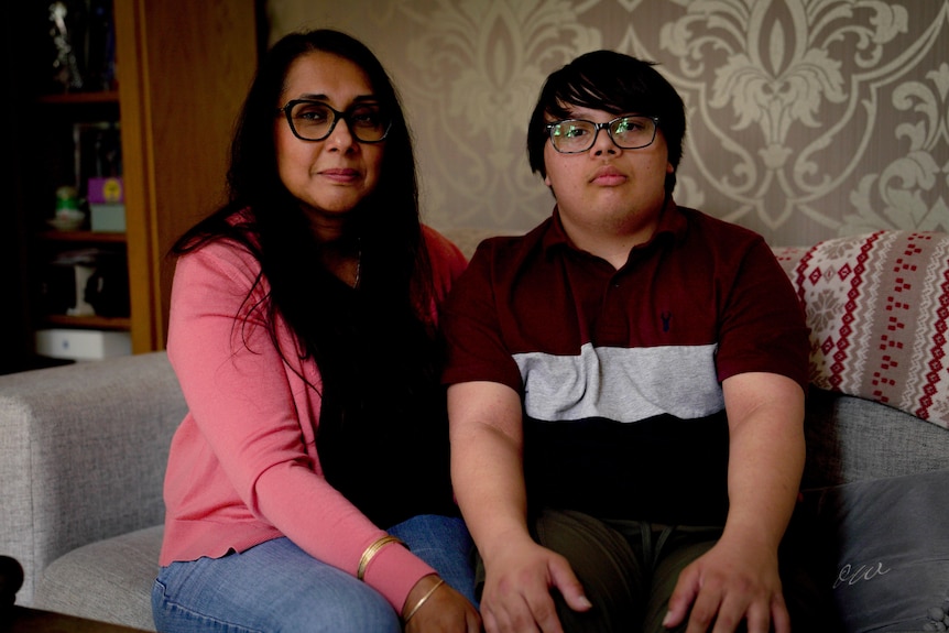 A mother and her teenage son sit on a sofa.