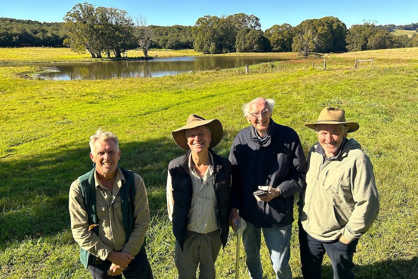 Four men in a paddock with dam in the background