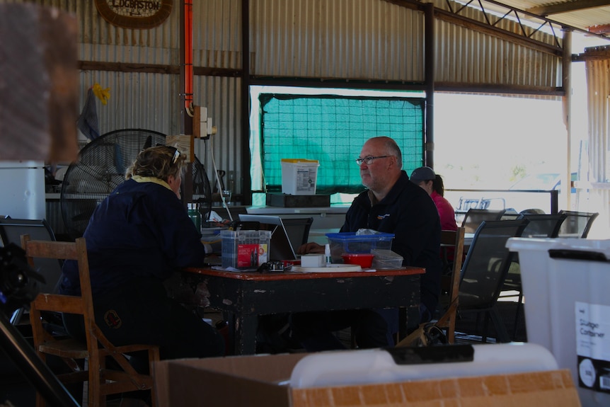 A man and a woman sitting at a table in a corrugated iron building surrounded by ecological equipment