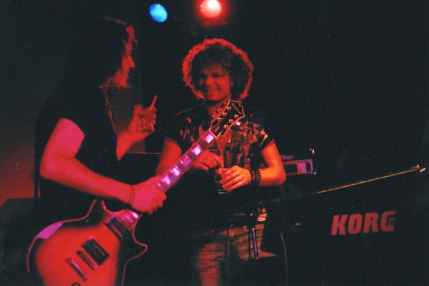 Band members hold instruments and drinks on stage.