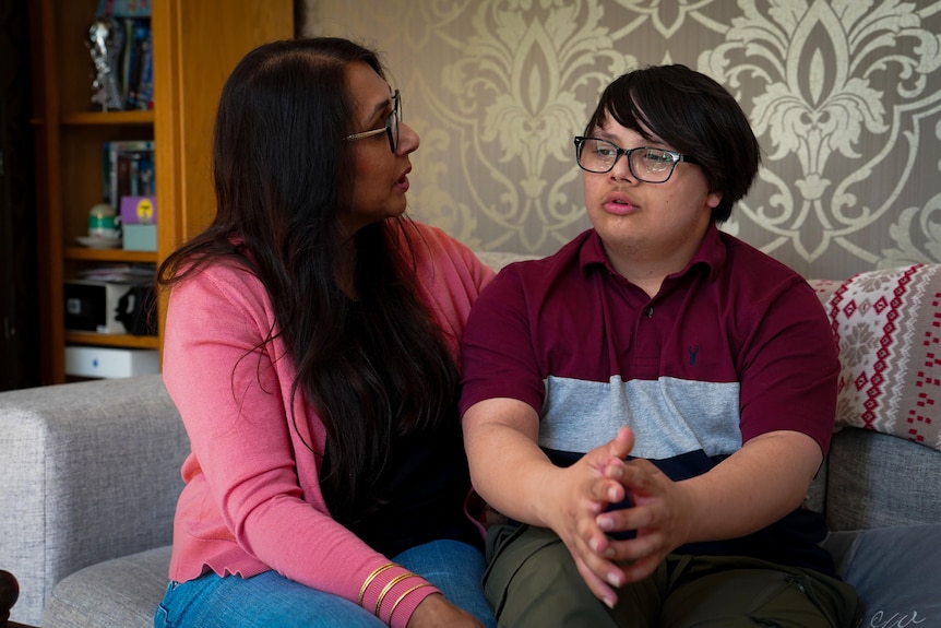 A mother and her teenage son talk to each other while sitting on a sofa.