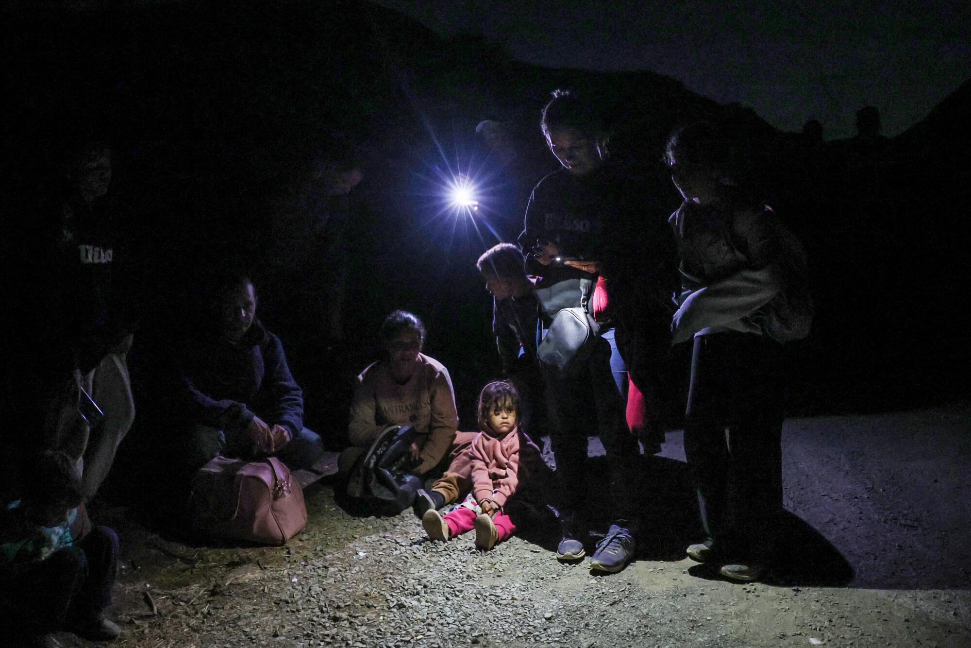 Adults and children sit on the ground at night.