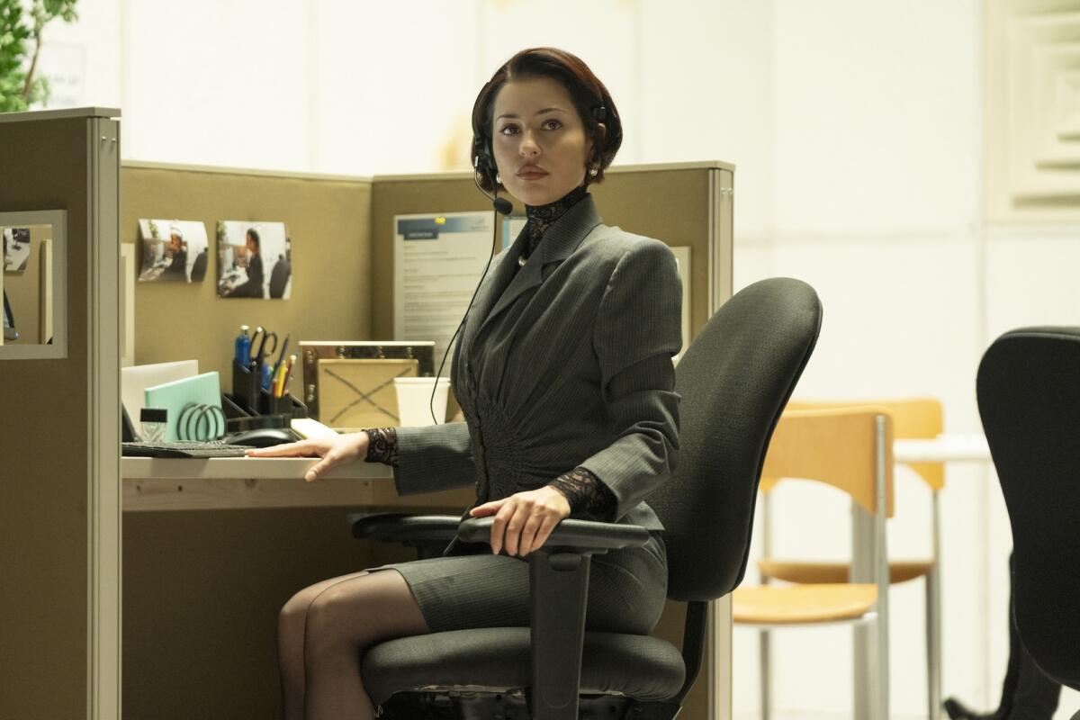 A woman sitting in an office cubicle wearing a suit and headset.