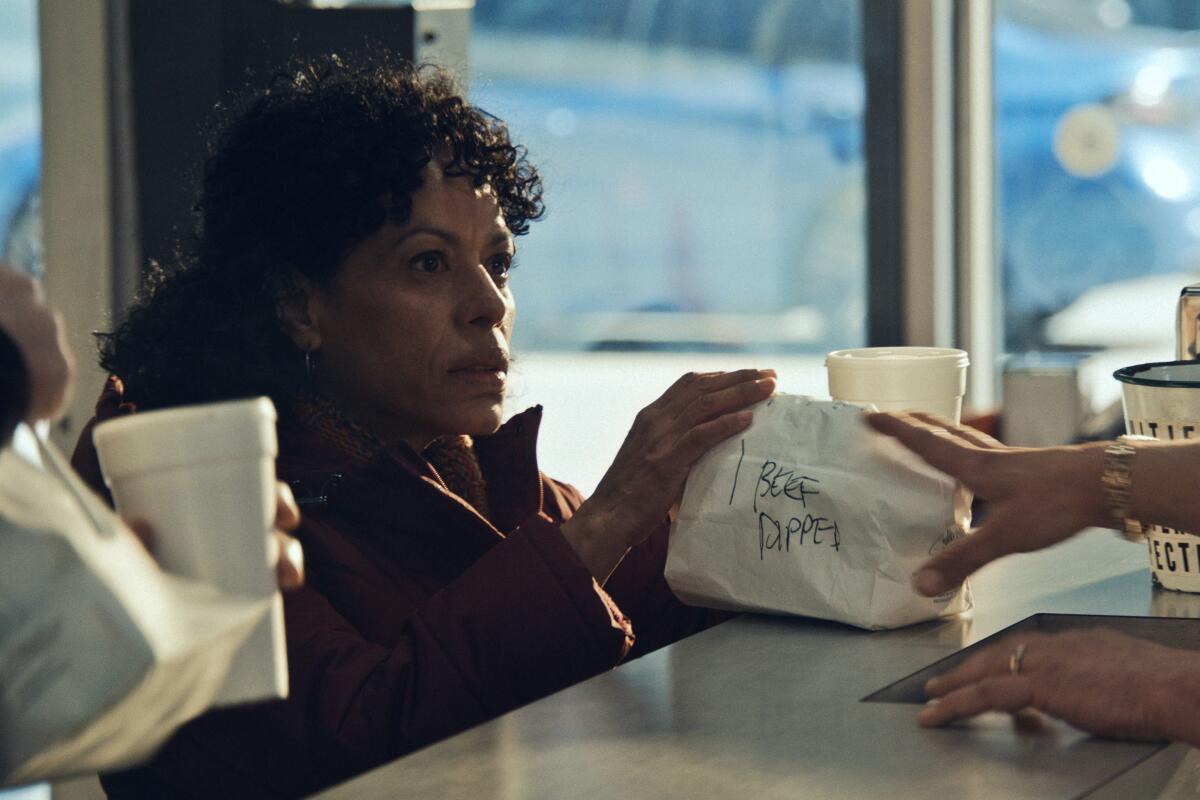 A woman at a counter grabbing a white lunch bag.