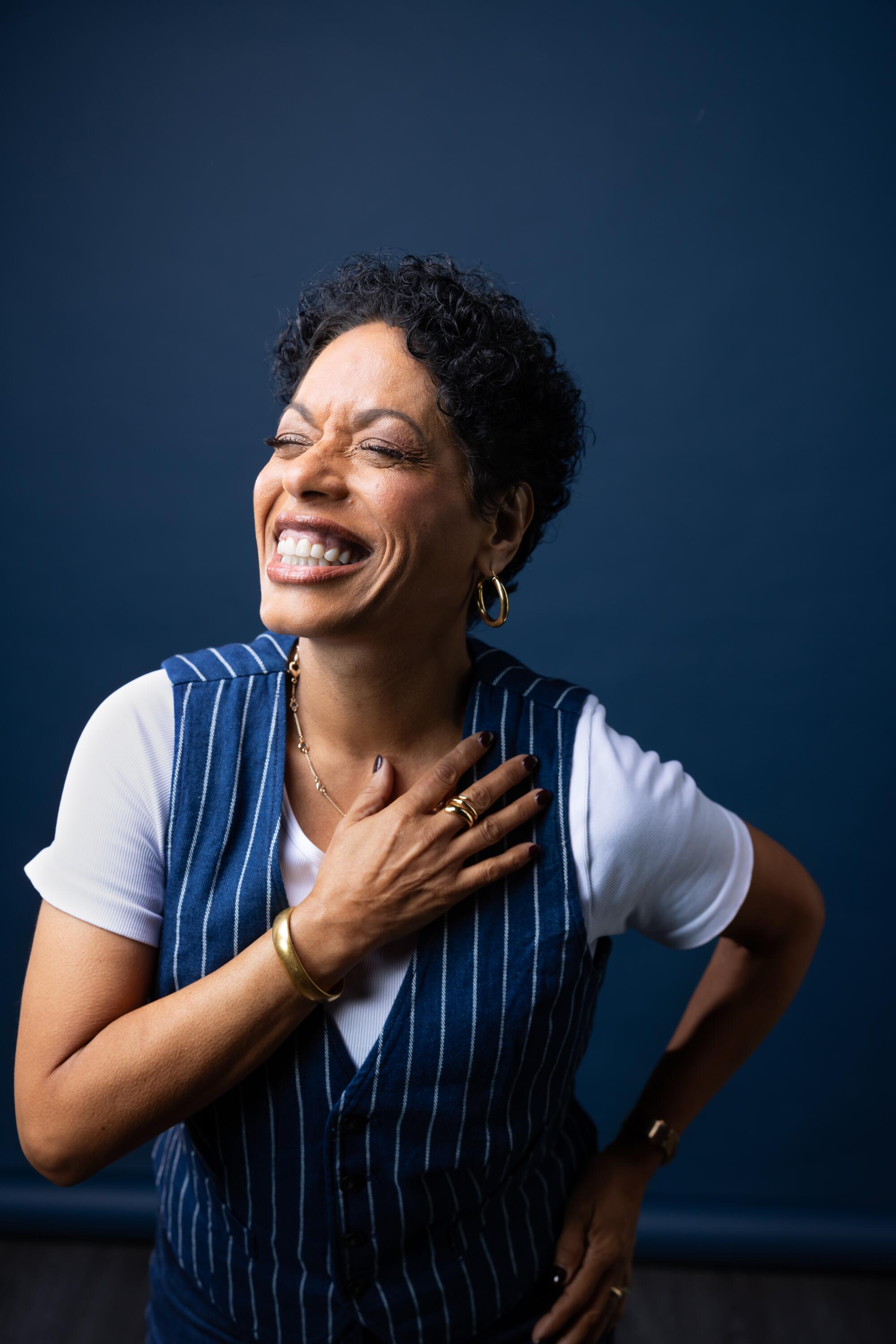 A woman with short hair smiles widely with her eyes closed