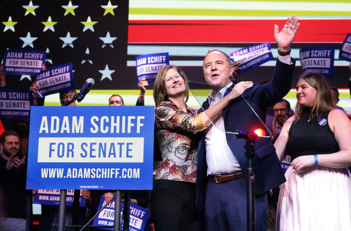 A woman has her hand on the shoulder of a man in a dark jacket, with one hand raised in celebration 