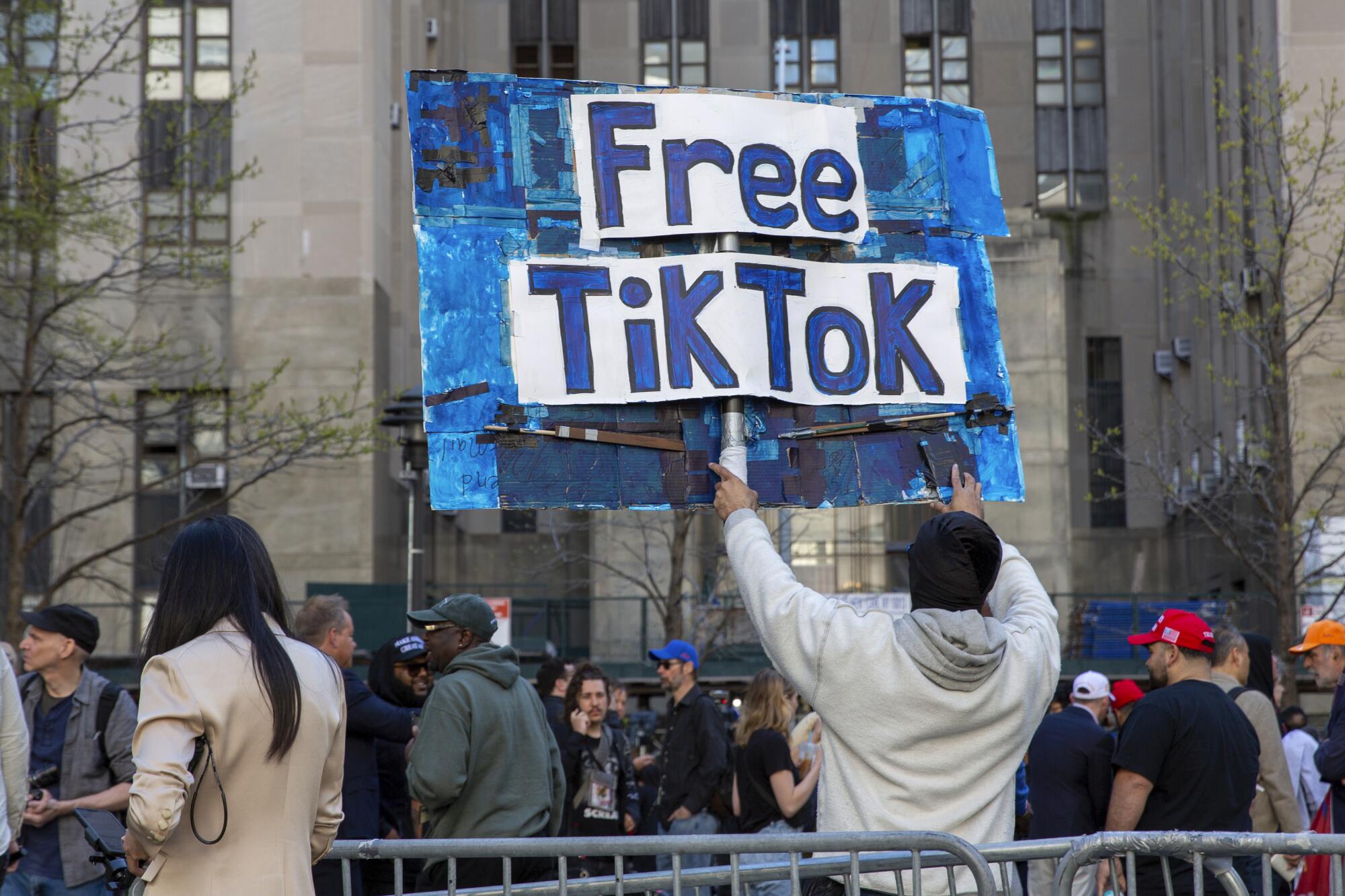 A man carries a Free TikTok sign in front of a building with a crowd of people