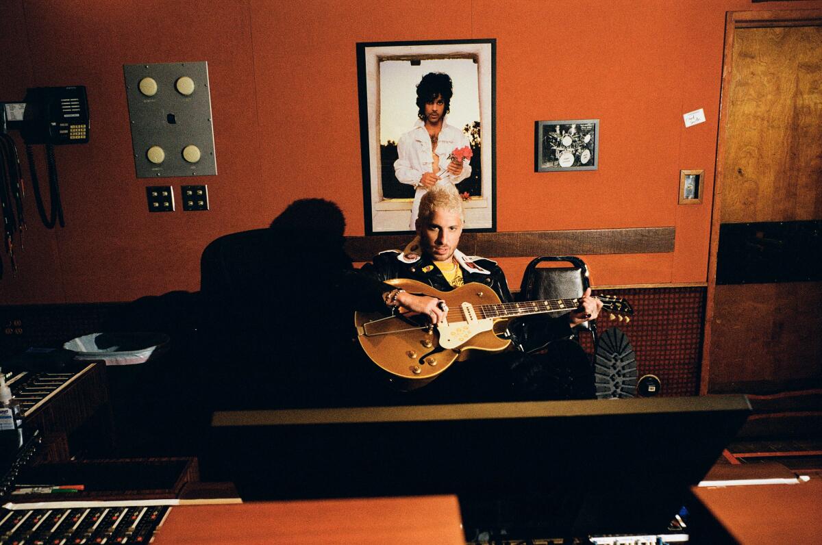 Man sitting in the recording studio with a guitar above a picture of Prince