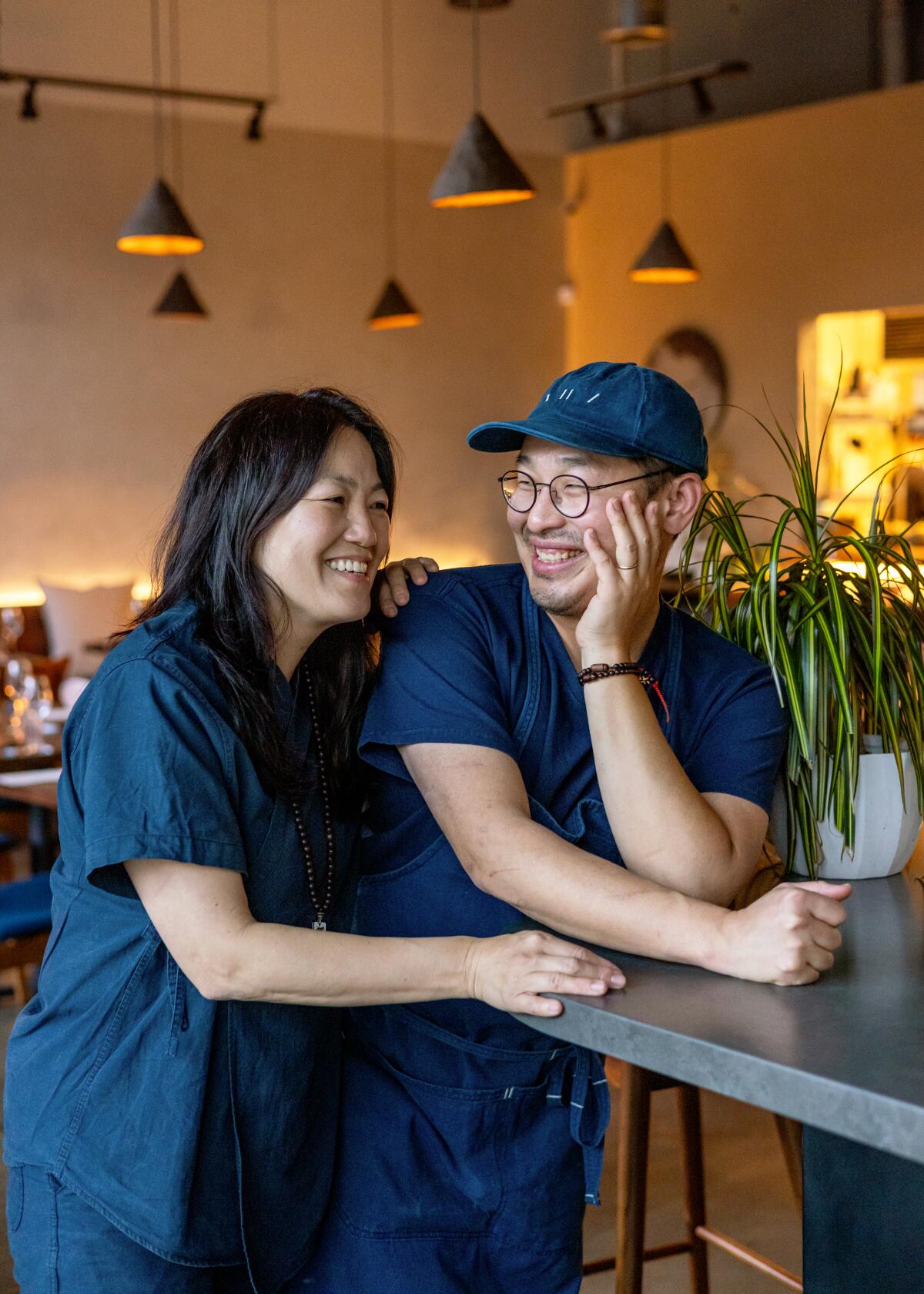 A smiling woman and man lean on a table.