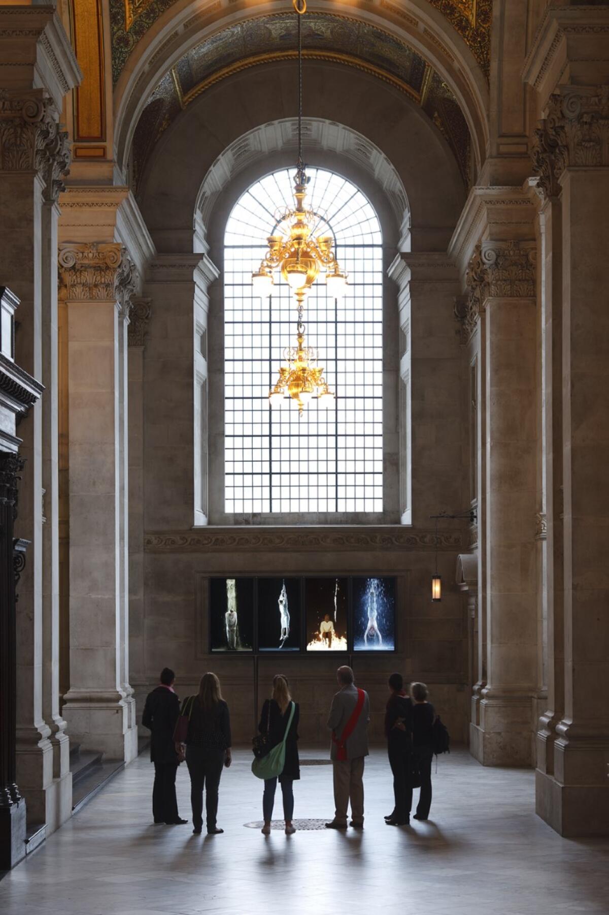 Patrons at a church look at an installation that shows human personifications of earth, air, fire and water.