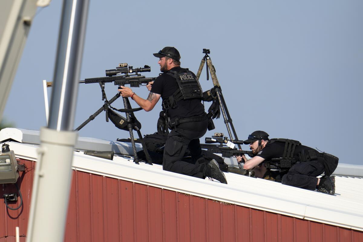 Police snipers on a rooftop return fire with scoped rifles mounted on tripods