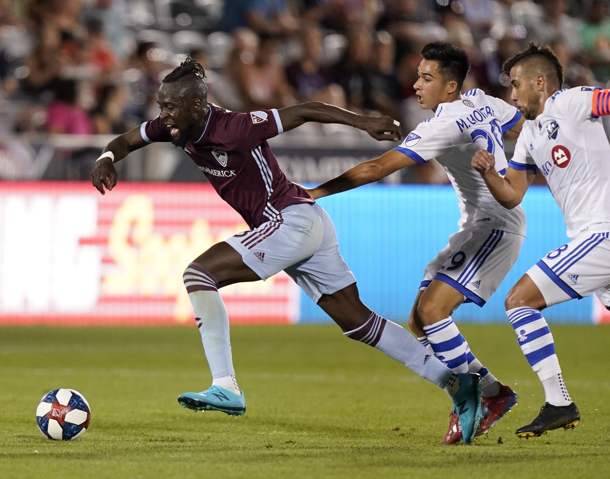 A soccer player bursts ahead of two defenders