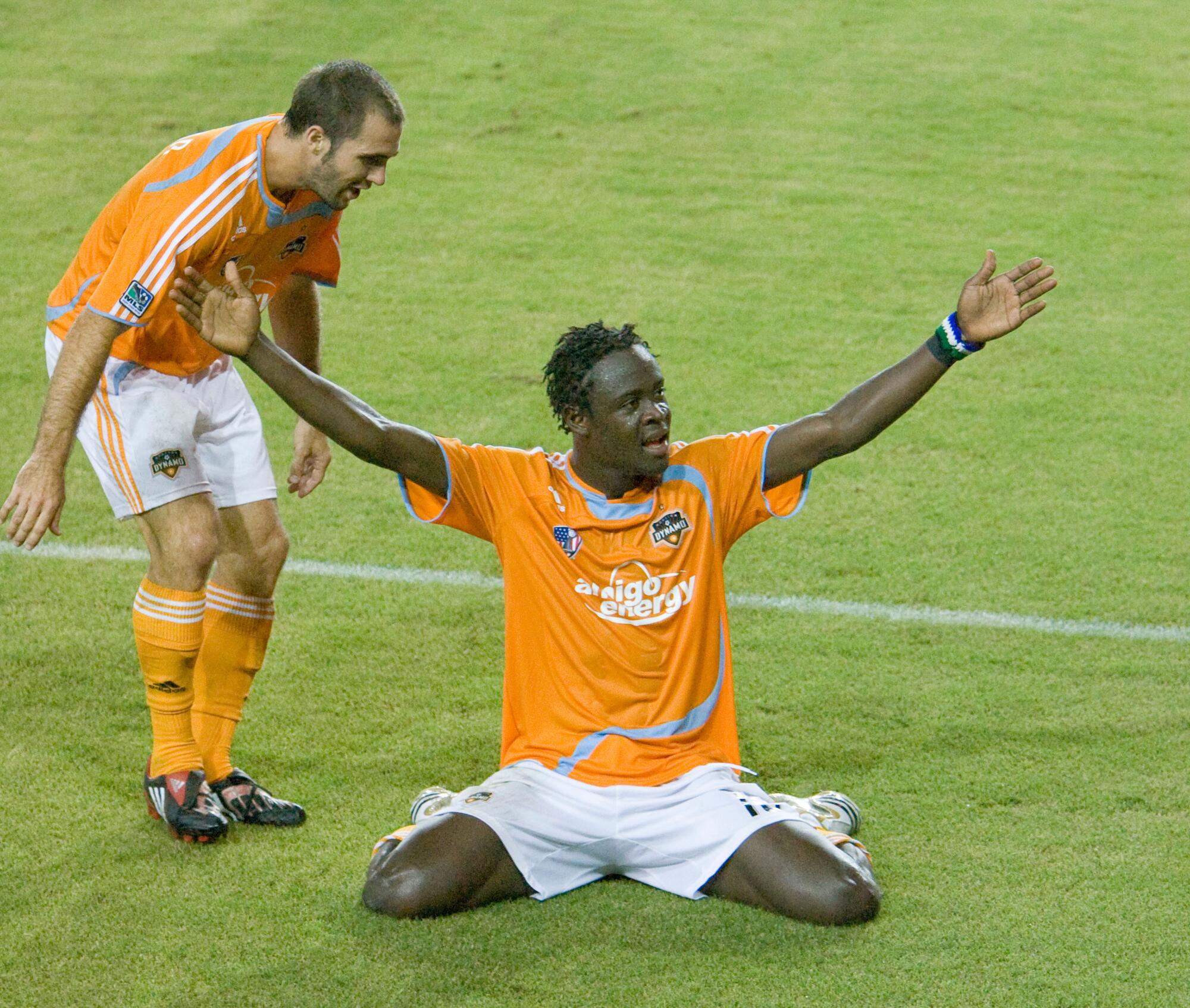 A soccer player slides on his knees after scoring a goal as a teammate watches K