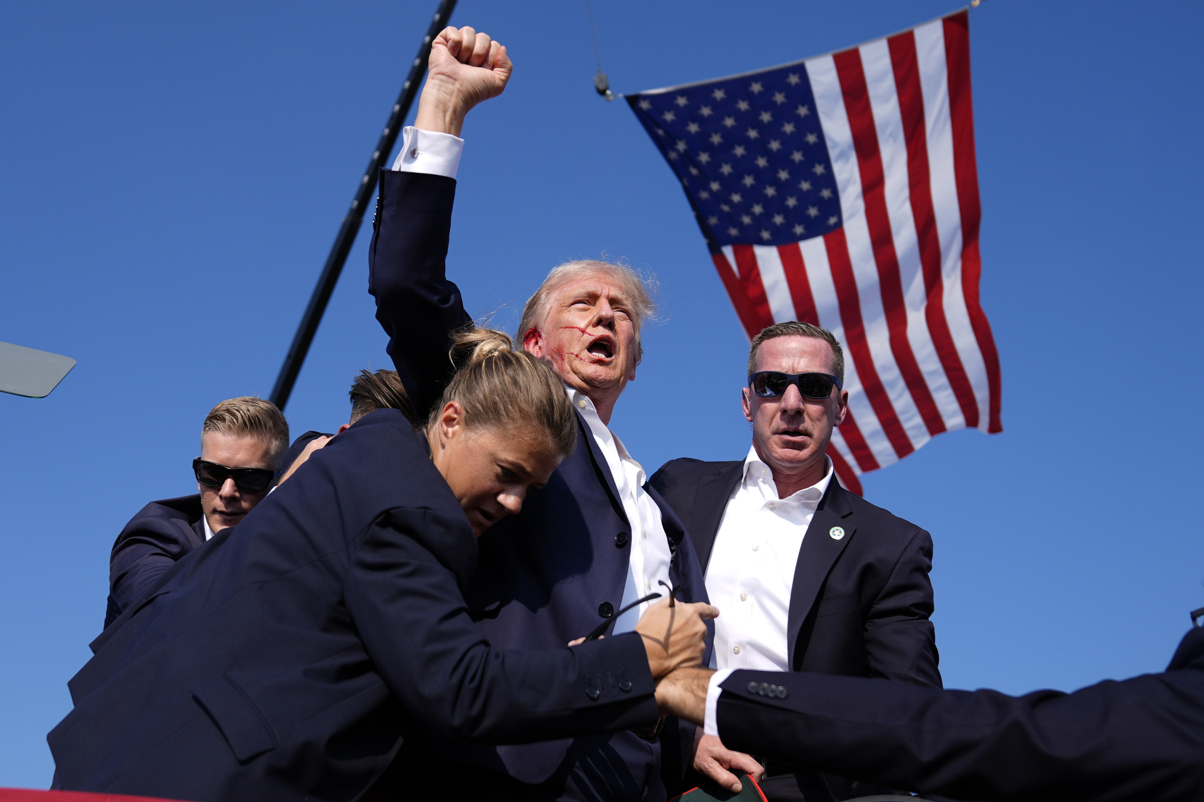 The former president - swarmed by Secret Service agents - with blood covering the right side of his face