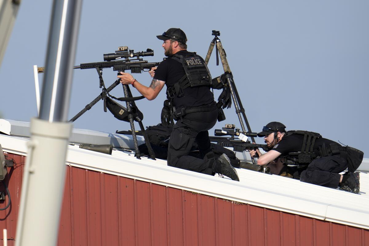 Two men in all-black clothing, one kneeling, the other lying on his stomach, wielding guns on tripods