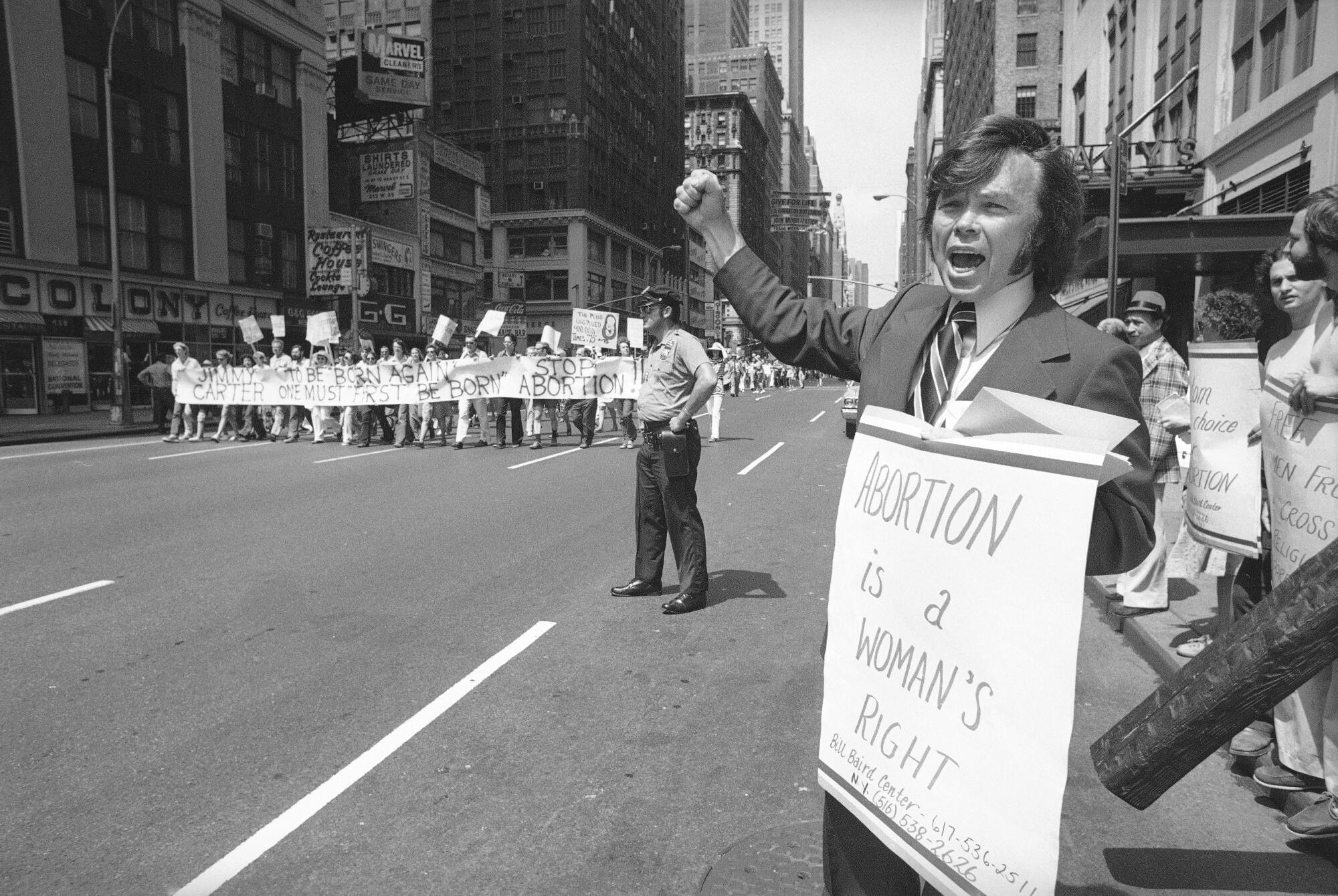 A man holds a sign that says, "Abortion is a woman's right," on a street.