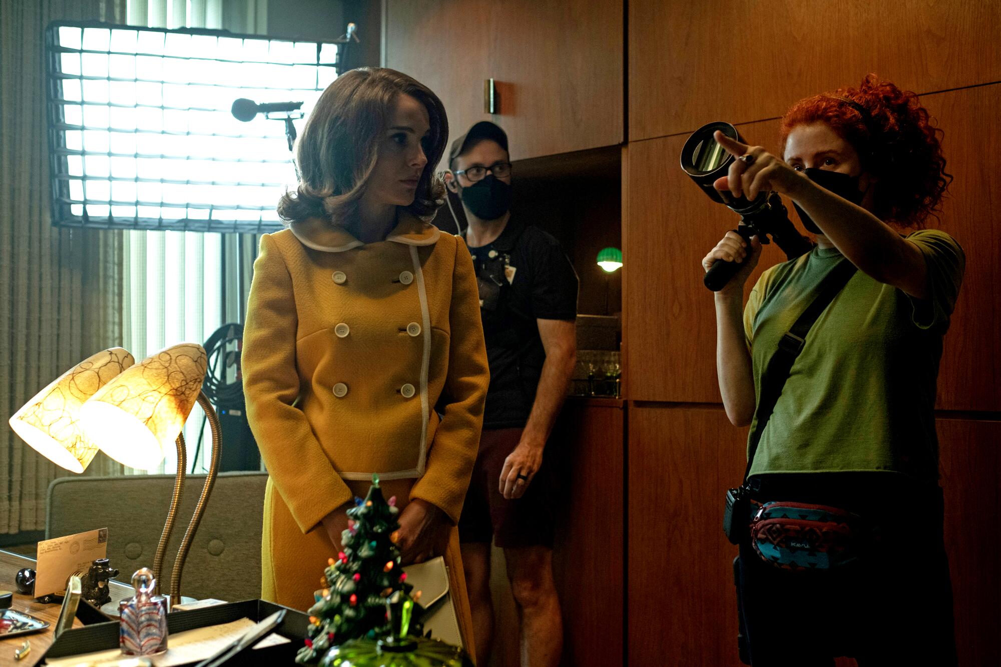 A woman in a yellow dress look at woman in a green shirt holding a camera.