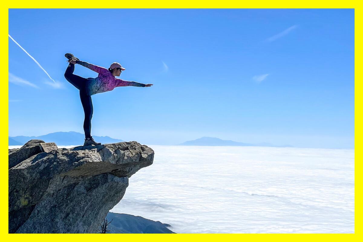 A woman holds the "dancer pose" on a rock that juts out above a misty expanse.