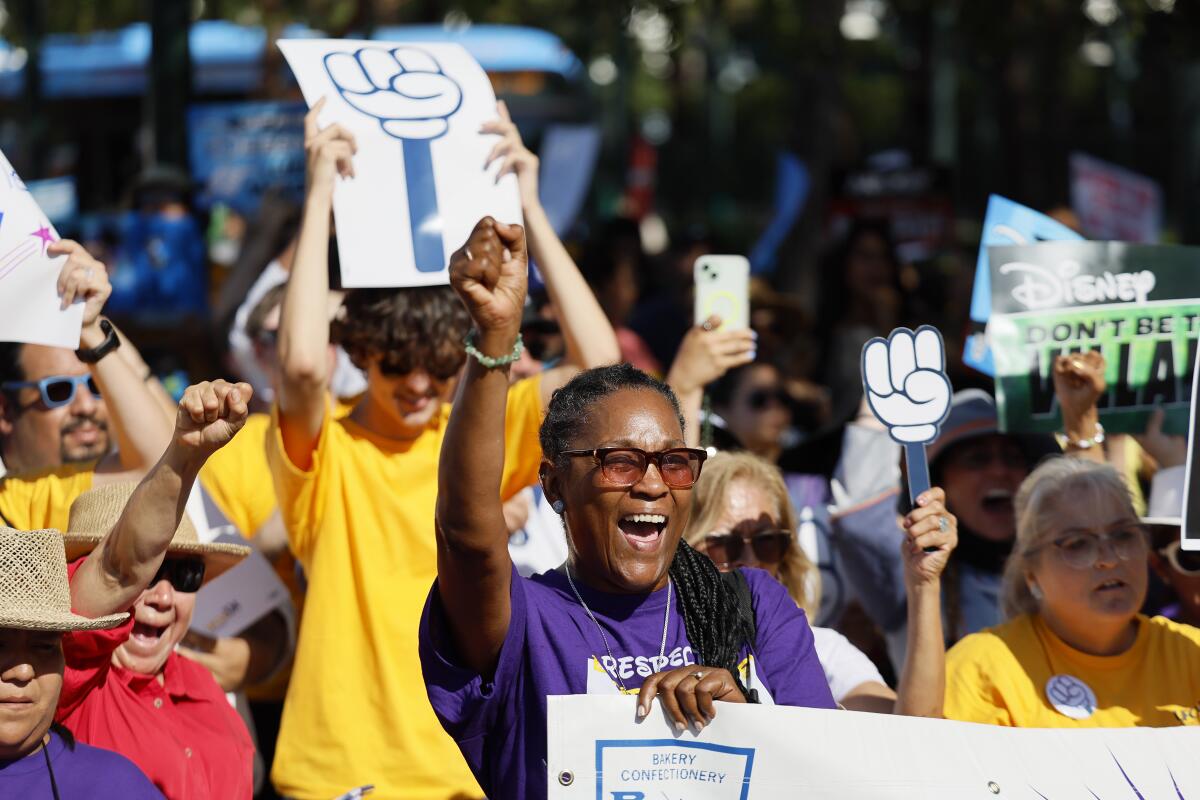 A woman raises her fist as other demonstrators march and carry picket signs.