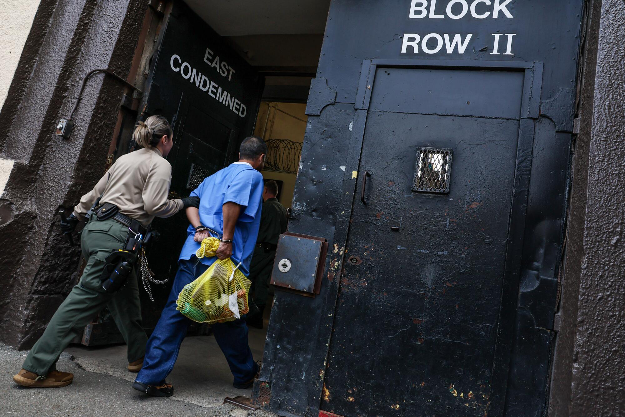 A guard leads a prisoner, his wrists shackled, into San Quentin's death row. 