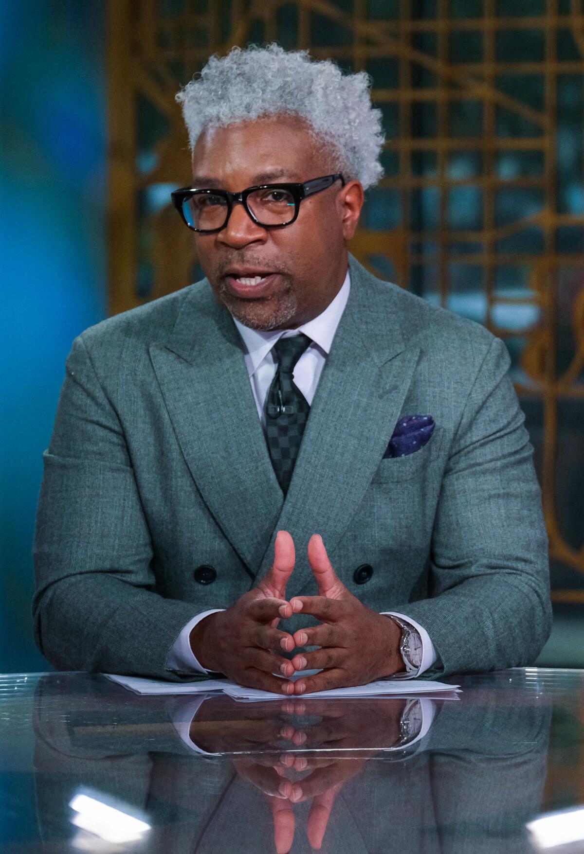 Cornell Belcher, in a suit, speaks while sitting 