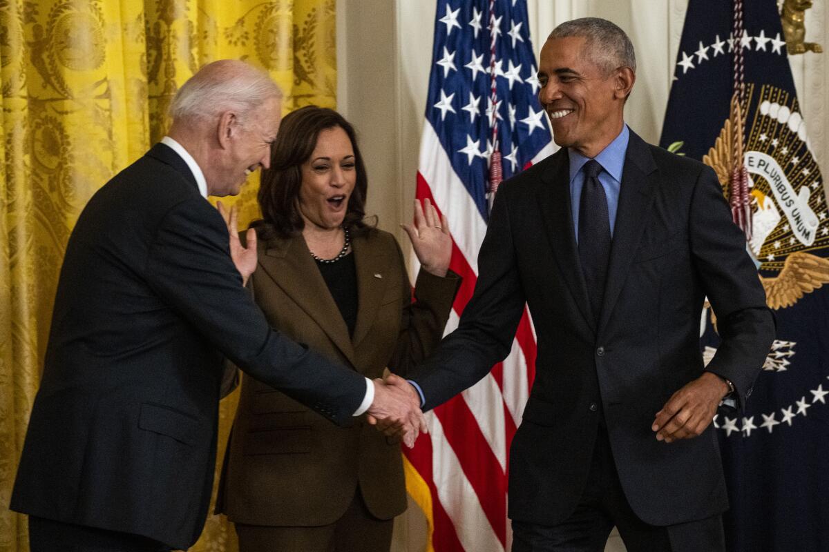 Biden and Obama shake hands as Kamala Harris looks on.