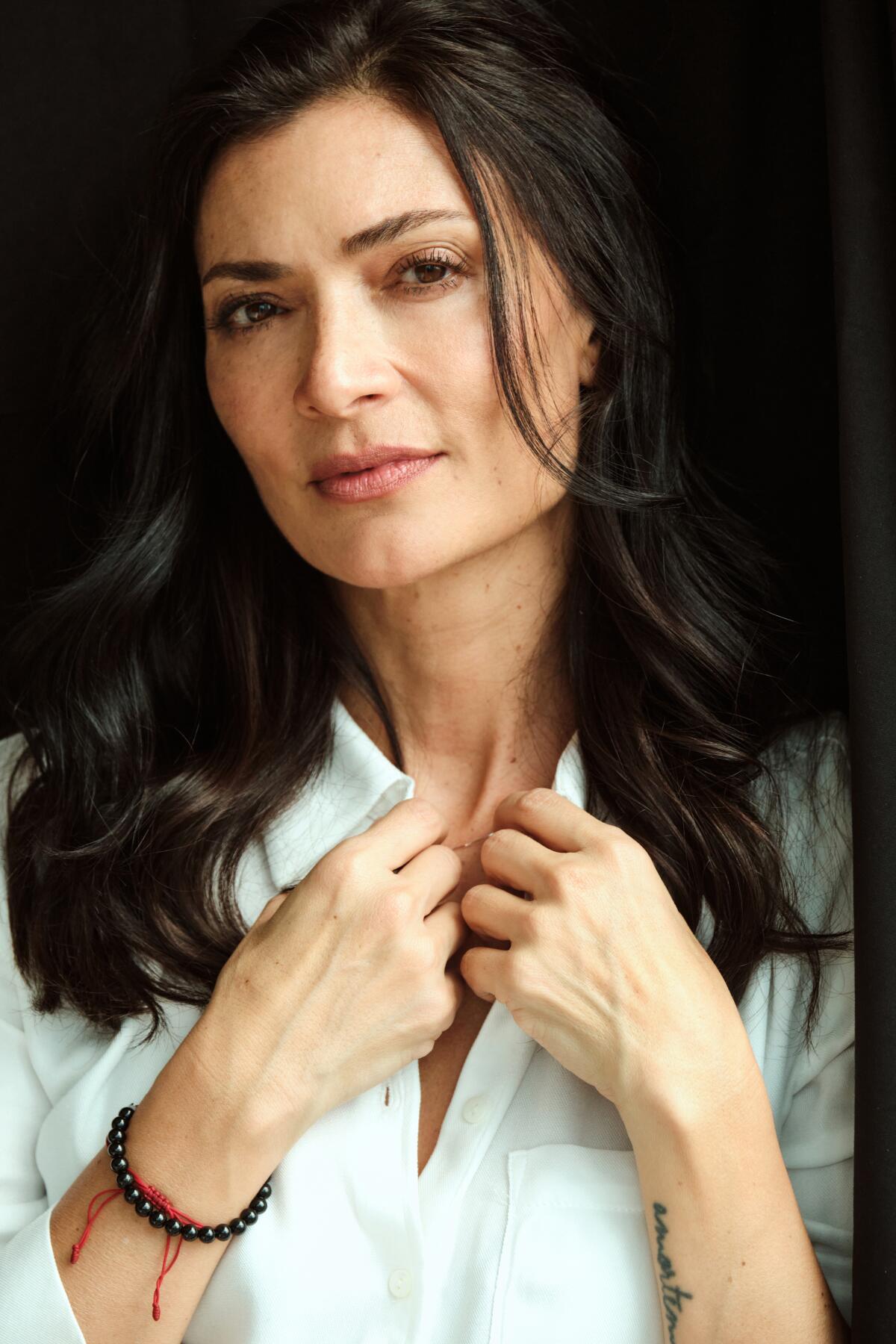 Ana Maria Orozco in a white shirt holding her hands at her collar.