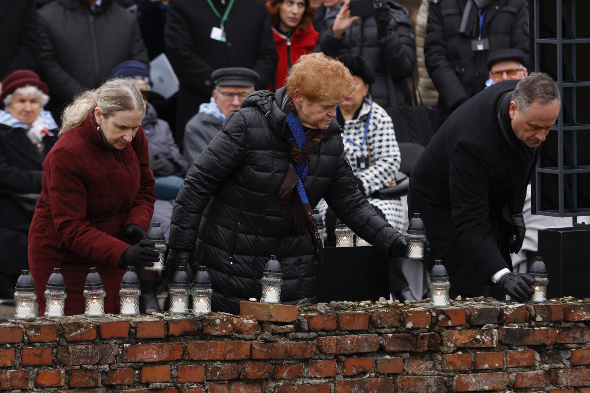 U.S. Second Gentleman, Doug Emhoff, right, and Deborah Lipstadt, center, place candles along a brick wall