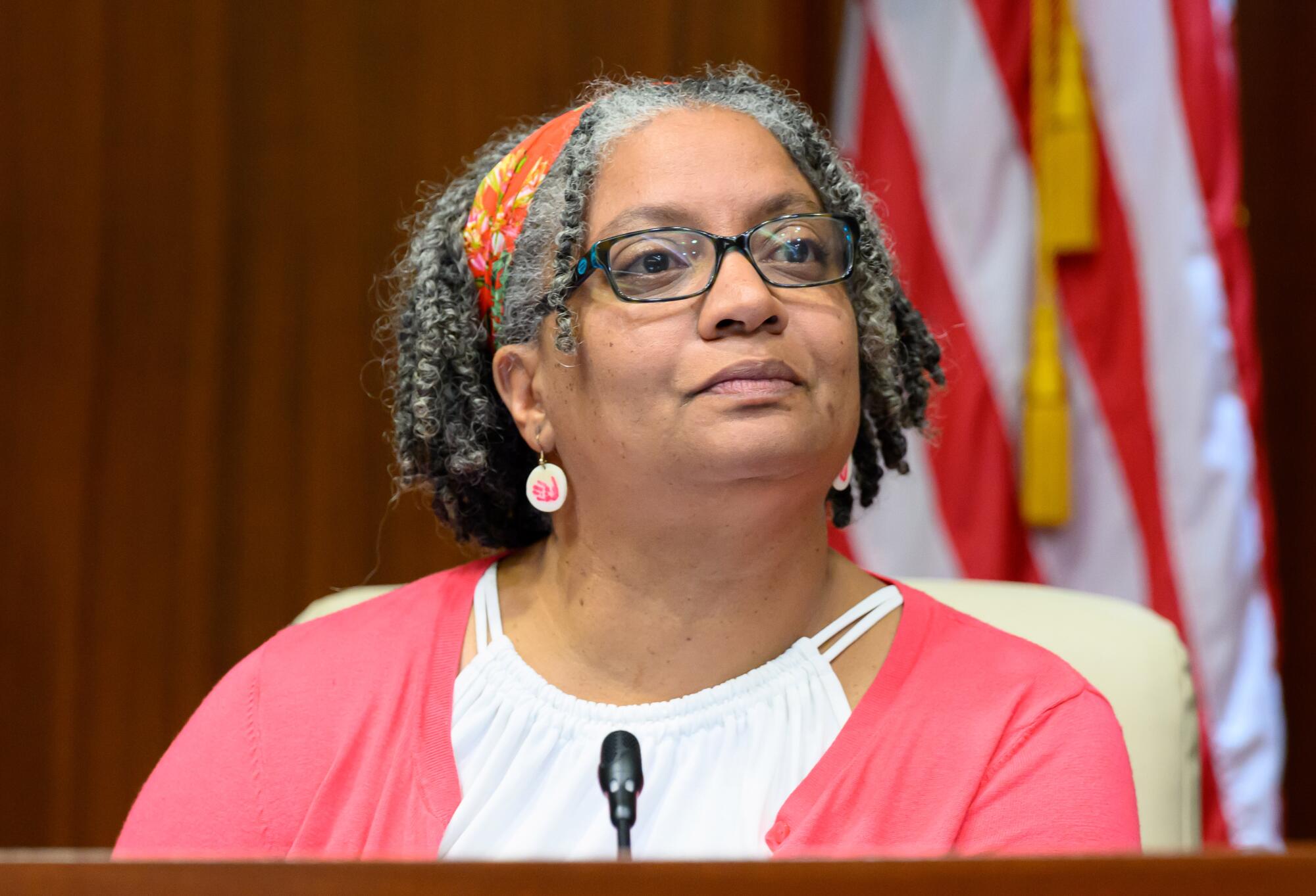 A woman in a pink sweater, with an American flag behind her.