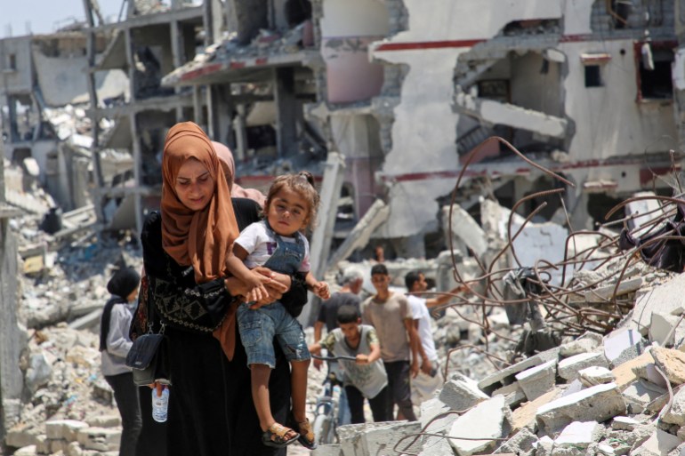 A Palestinian woman holds her daughter as she walks past the rubble of houses destroyed by the Israeli military in Khan Younis