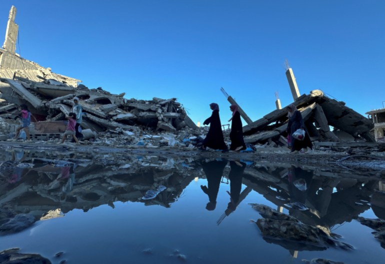 Palestinians walk past the rubble of houses destroyed in Israeli strikes, 