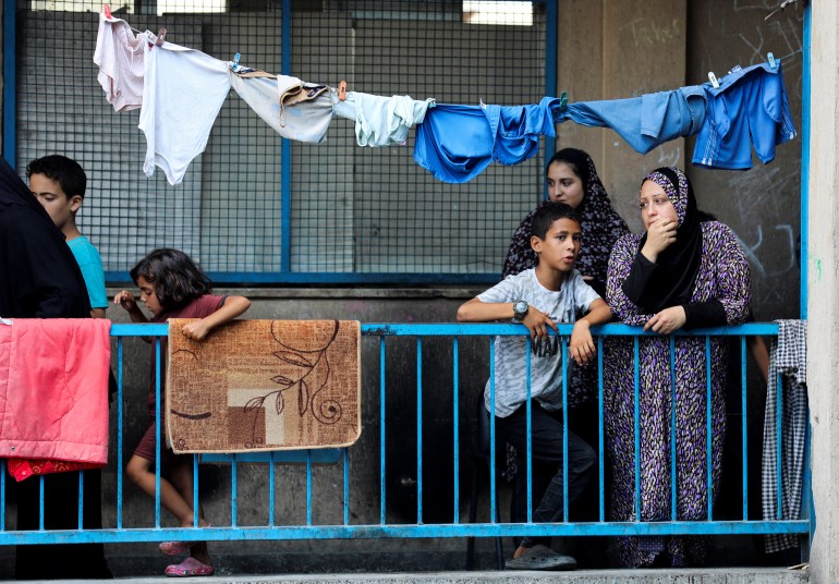 Palestinians stand on a balcony as others gather at the site of an Israeli air strike on a UN school sheltering displaced people