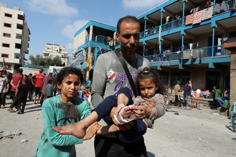 A Palestinian man carries a wounded child as people gather at the site of an Israeli air strike on a UN school sheltering displaced people