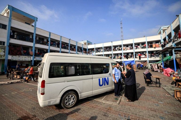 A man speaks with a worker of the United Nations Relief and Works Agency for Palestine Refugees (UNRWA) agency outside one of their vehicles parked in the playground of an UNRWA-run school that has been converted into a