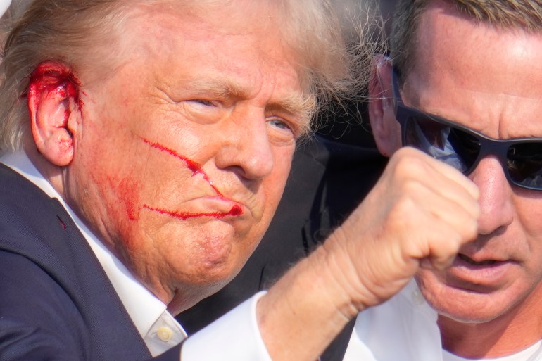 Republican presidential candidate former President Donald Trump gestures as he is surrounded by U.S. Secret Service agents as he is helped off the stage at a campaign rally in Butler