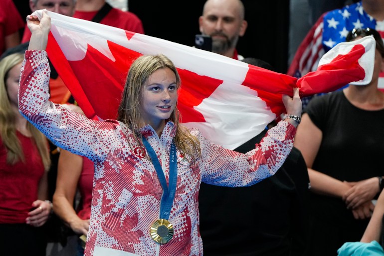 Summer McIntosh, of Canada, holds her national flag after winning the women's 400-meter individual medley final at the 2024 Summer Olympics, Monday, July 29, 2024, in Nanterre, France. (AP Photo/Matthias Schrader)