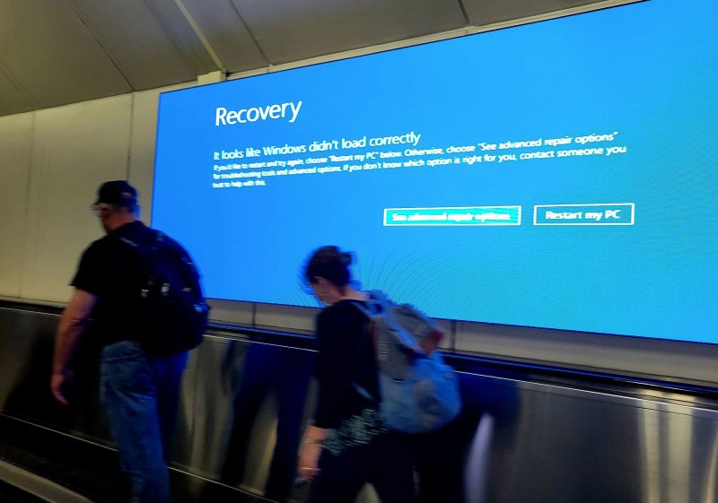 Travelers walk past a screen displaying a Microsoft Windows error message at Dulles International Airport in Washington, D.C. on Saturday. Chaos from Friday's global tech outage moved into a second day at airports across the United States with more than 8,000 flights canceled or delayed. File Photo by Pat Benic/UPI