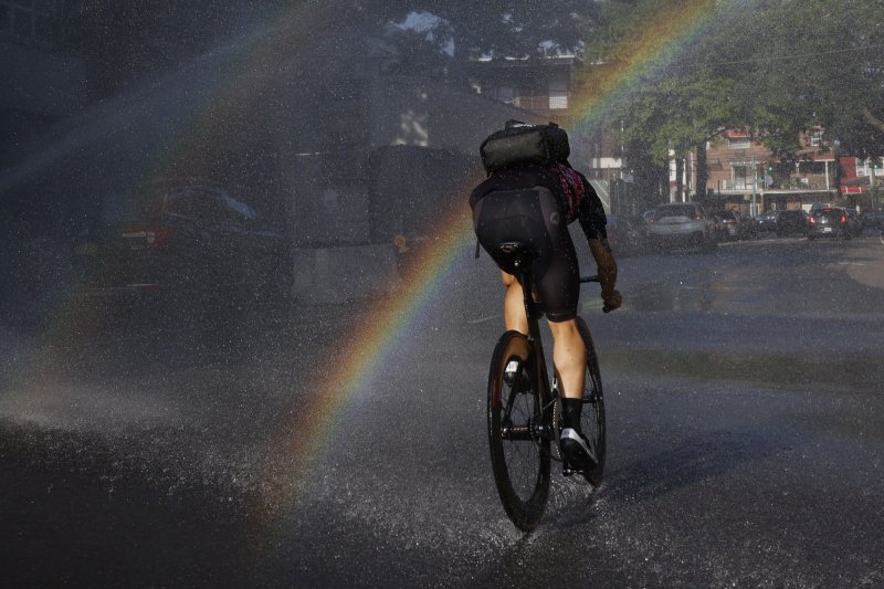 A cyclist pedals through splashing waters from an opened fire hydrant during dangerously hot weather in the Queens borough in New York City on July 26, 2023. A new report said the world faced record-high temperatures for 12 months straight. File Photo by John Angelillo/UPI