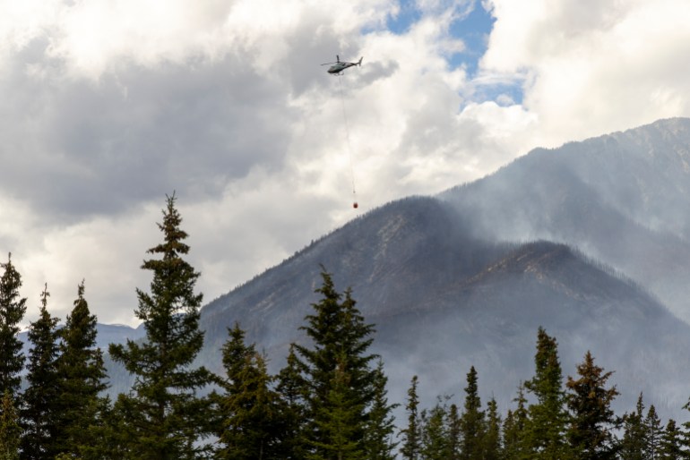 A helicopter carries water toward the Chetamon Mountain wildfire in Jasper National Park in Jasper, Alberta, Canada