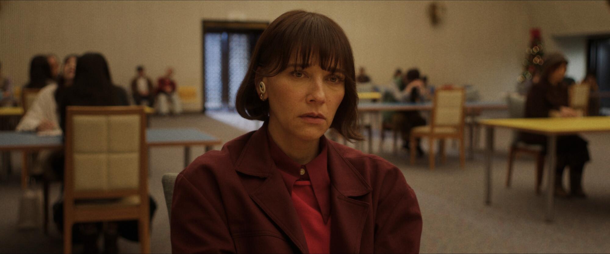 A woman with short hair in a maroon jacket and shirt sitting at a table.