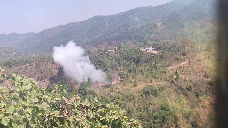 White smoke rising after a Myanmar military attack on Shan state. The area is forested and hilly.