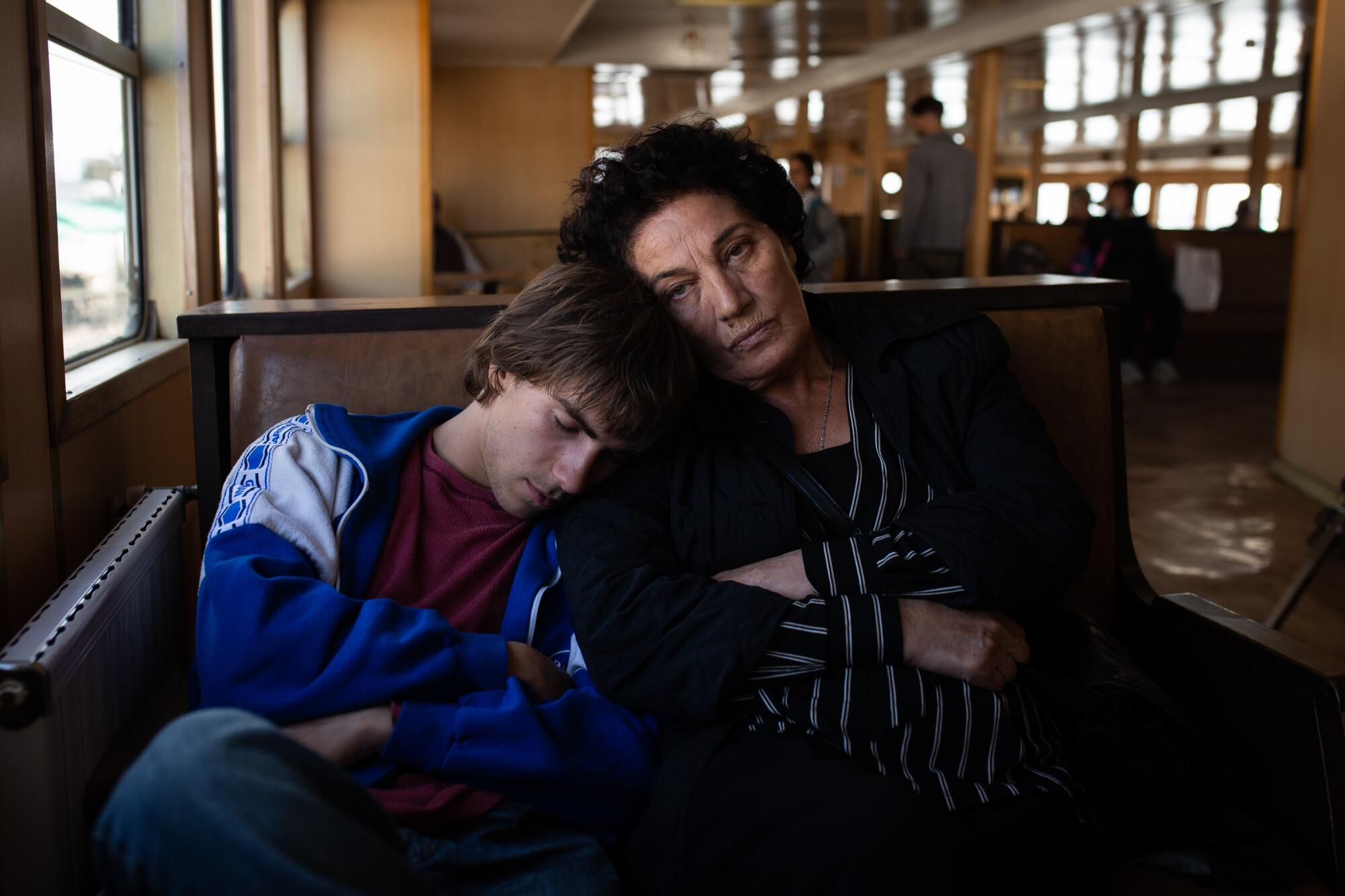 A young man rests his head on a woman's shoulder.