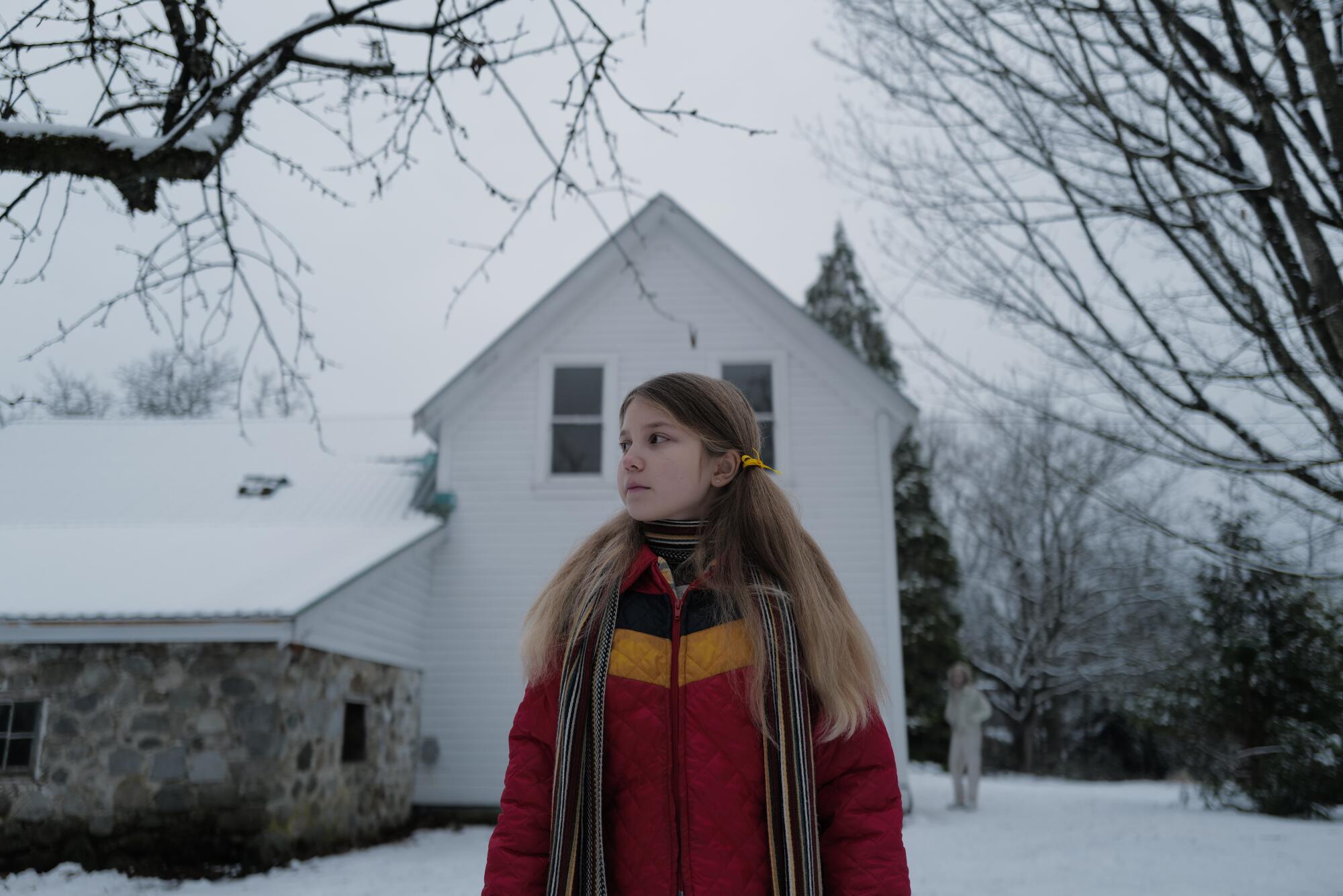 A girl stands on a snowy lawn while behind her, a man in white watches.